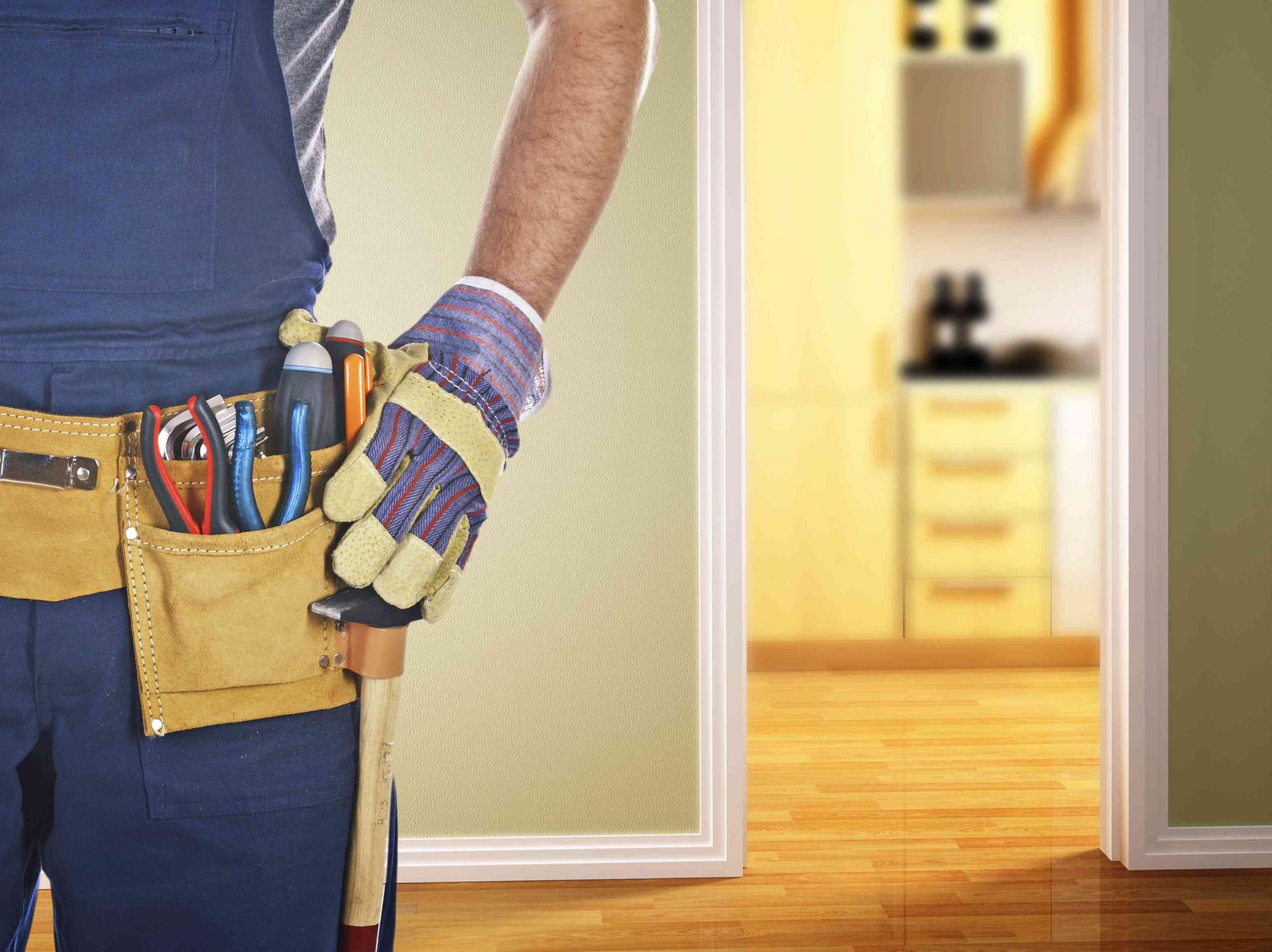 A carpenter has a tool belt with pliers and screwdrivers. He has his gloves on and his hand is on the side of the pocket of this tool belt.