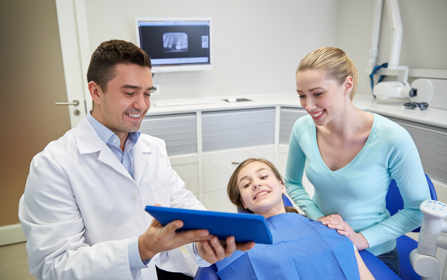 A dentist and his assistant are showing a young patient her x-rays.