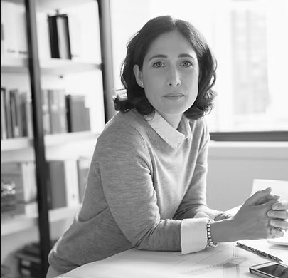 A woman at a city office sits at a desk with her hands clamped together, looking towards the camera optimistically.